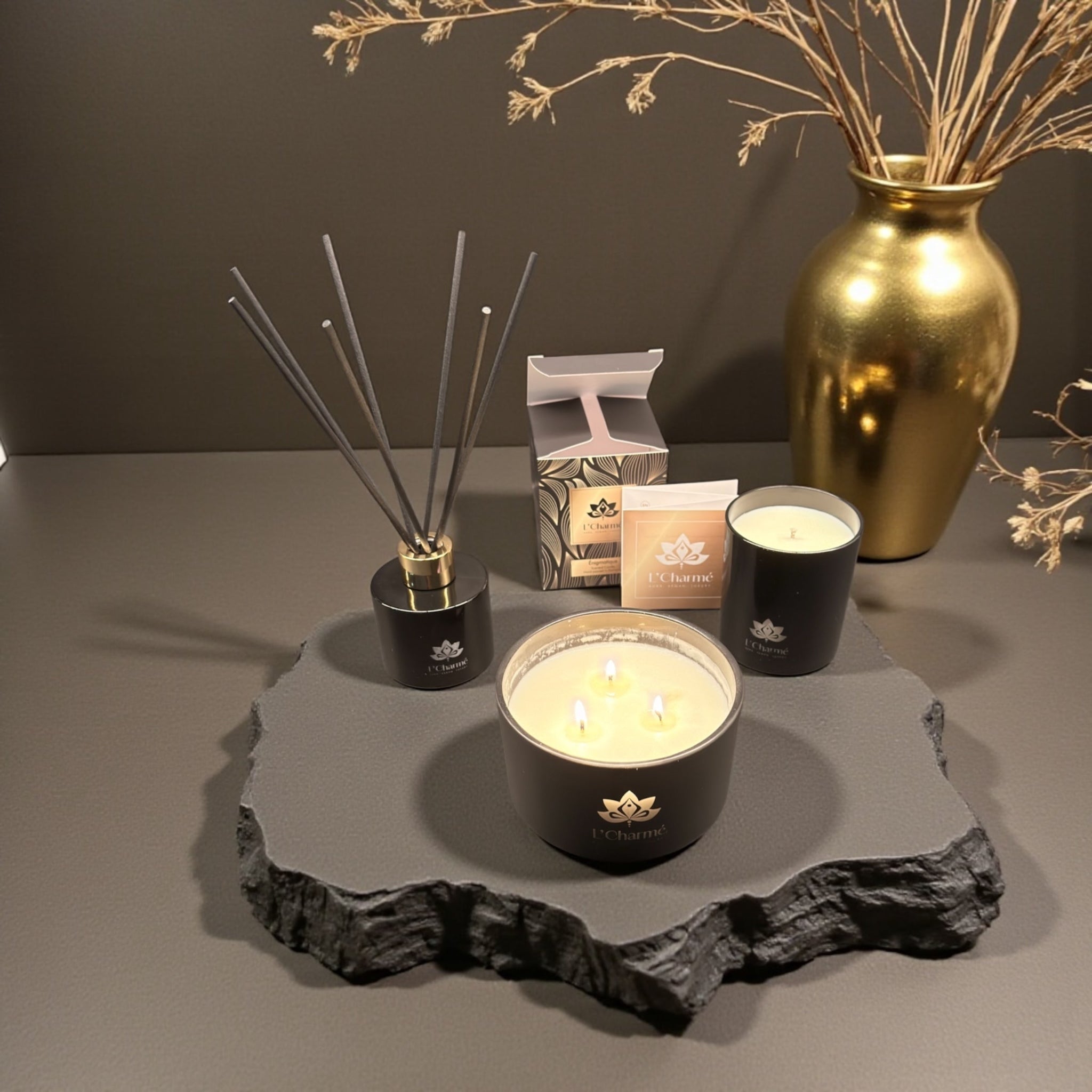 Duftkerzen und Duftstäbchen von L’Charmé mit Verpackung auf einer grauen Natursteinplatte in elegantem Arrangement