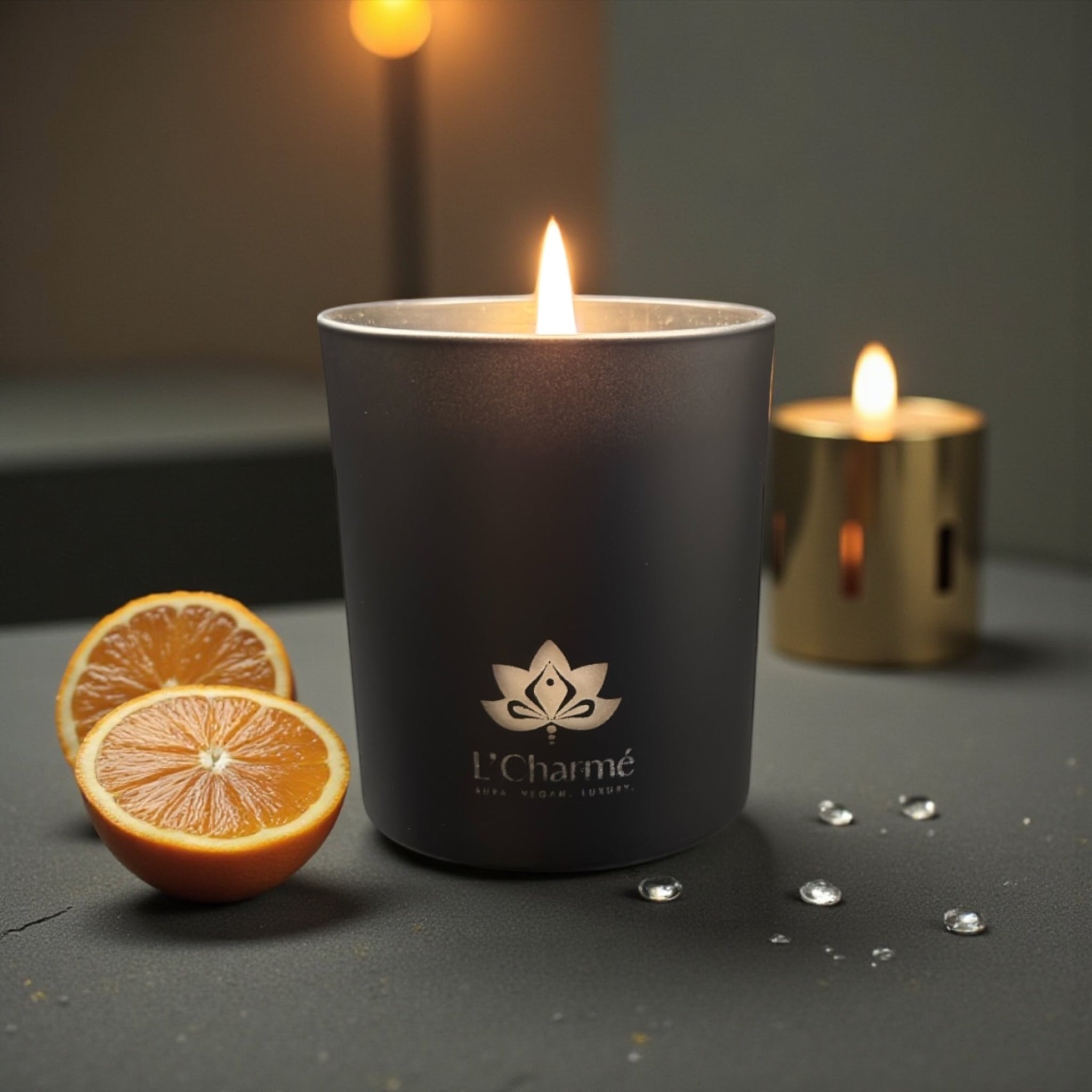 Schwarze brennende Duftkerze Mandarine Éclat von L’Charmé auf dunkler Oberfläche mit Orangenscheiben in elegantem Ambiente