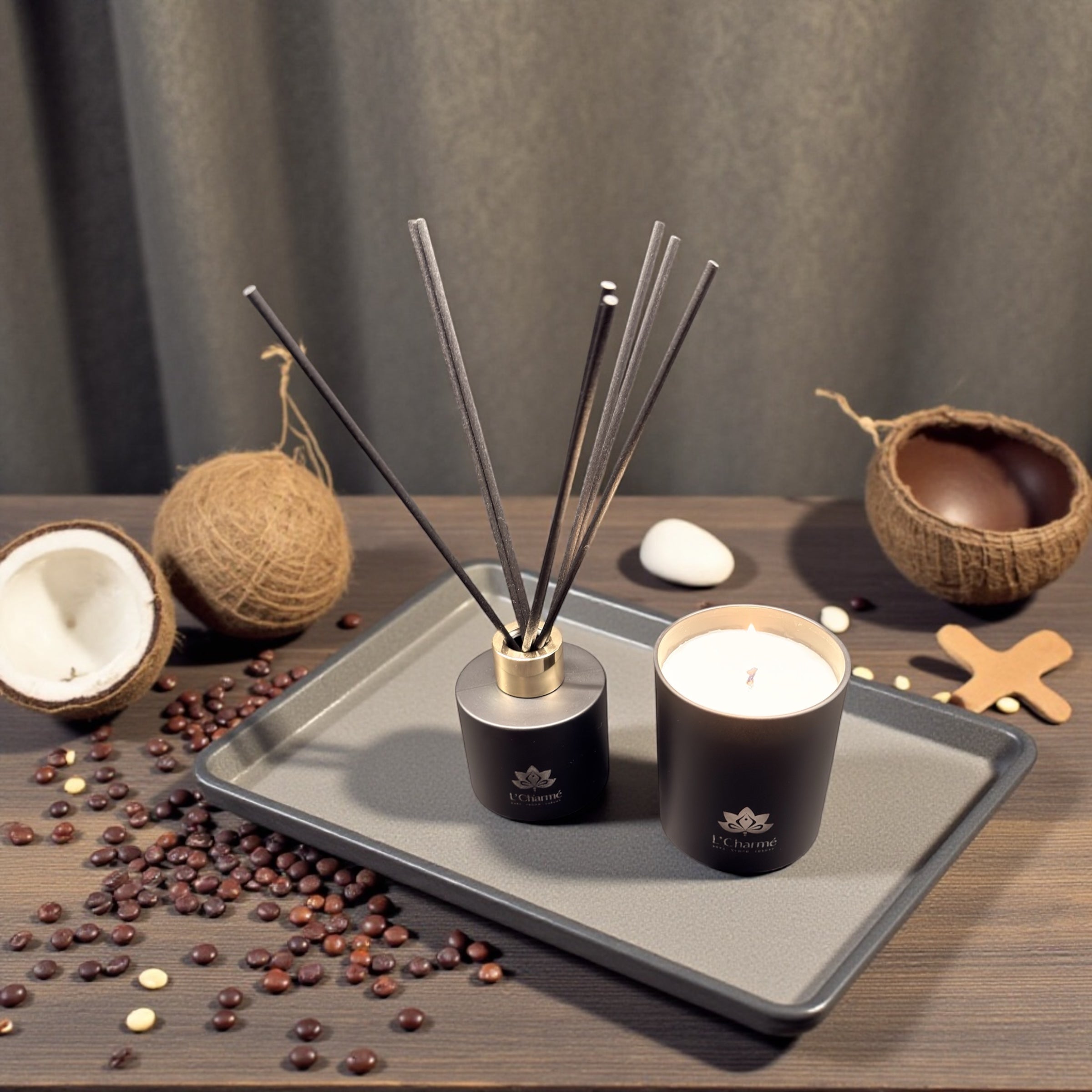 Schwarzer Duftdiffuser und brennende Duftkerze von L’Charmé auf einem grauen Tablett mit Kokosnuss und Kaffeebohnen in elegantem Arrangement