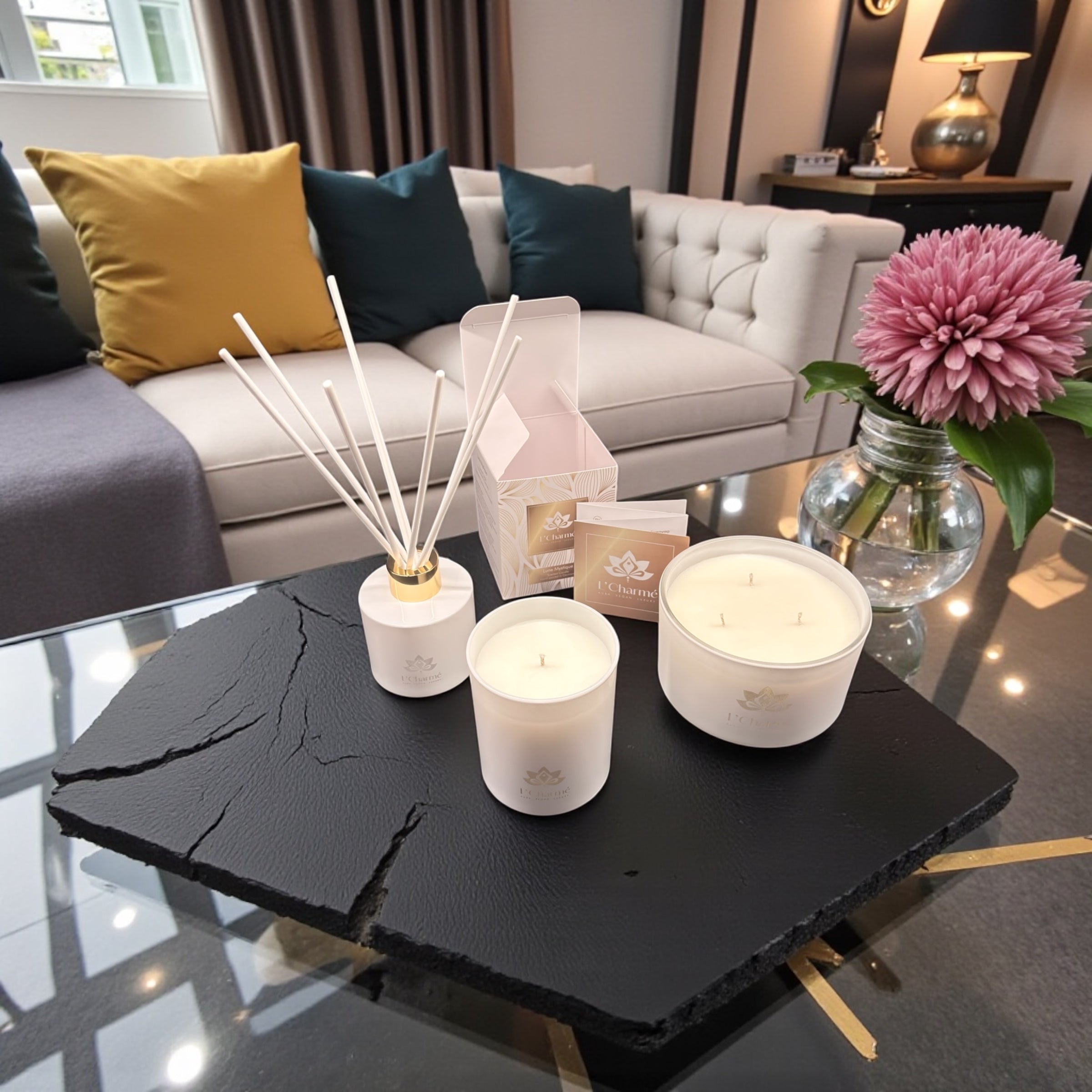 Weiße Dreidocht-Duftkerze von L’Charmé auf einer schwarzen Natursteinplatte neben einer rosa Blumenvase in elegantem Wohnambiente