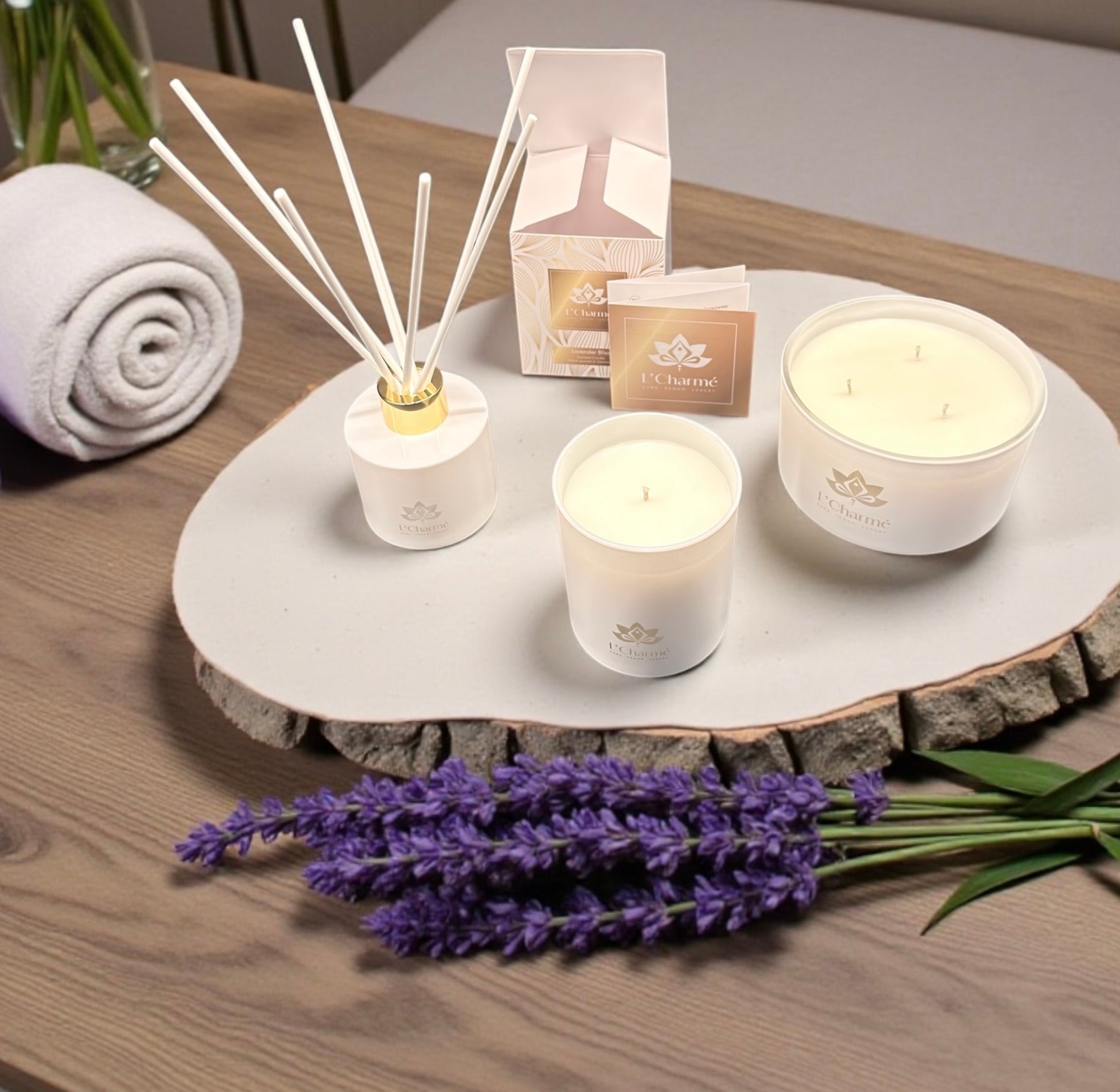 Weiße Duftkerzen und Duftstäbchen von L’Charmé mit Verpackung auf einem Holztisch mit Lavendel in elegantem Arrangement