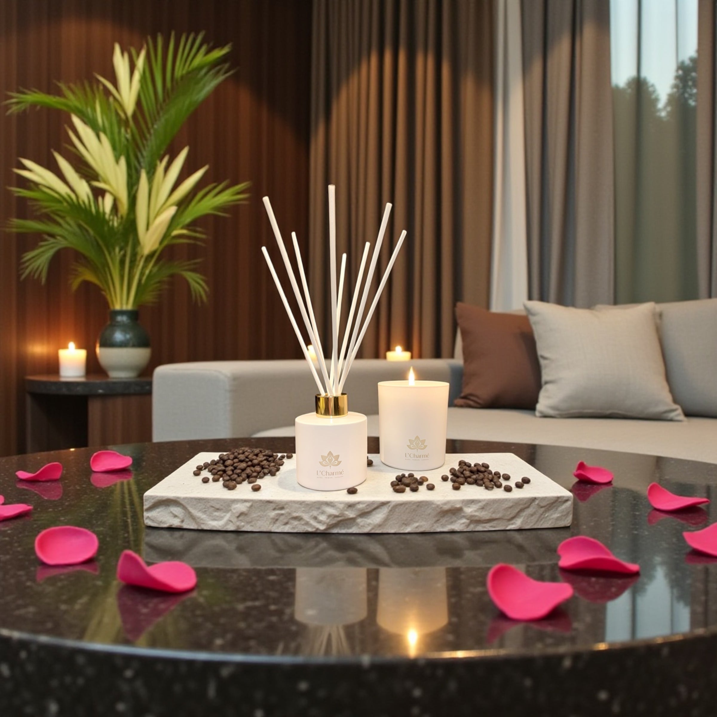 Weißer Duftdiffuser und brennende Duftkerze von L’Charmé auf einer Steinplatte mit Kaffeebohnen und rosa Rosenblättern im eleganten Wohnraum