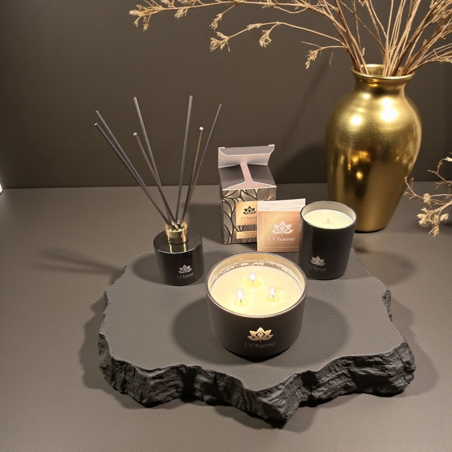Duftkerzen und Duftstäbchen von L’Charmé mit Verpackung auf einer grauen Natursteinplatte in elegantem Arrangement