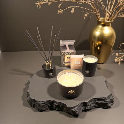Duftkerzen und Duftstäbchen von L’Charmé mit Verpackung auf einer grauen Natursteinplatte in elegantem Arrangement