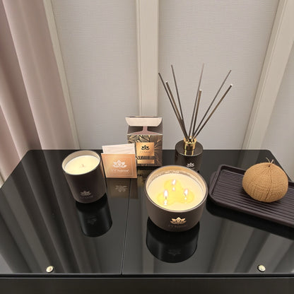 Duftkerzen und Duftstäbchen von L’Charmé mit Verpackung auf einem schwarzen Glastisch in elegantem Arrangement