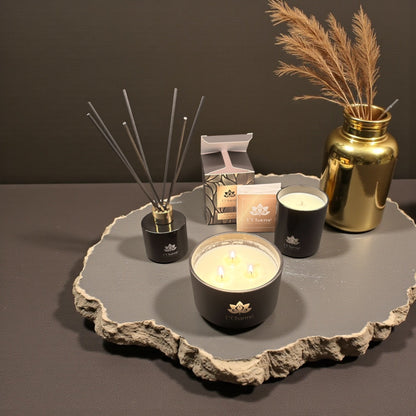 Duftkerzen und Duftstäbchen von L’Charmé mit Verpackung auf einer schwarzen Marmorplatte in elegantem Arrangement