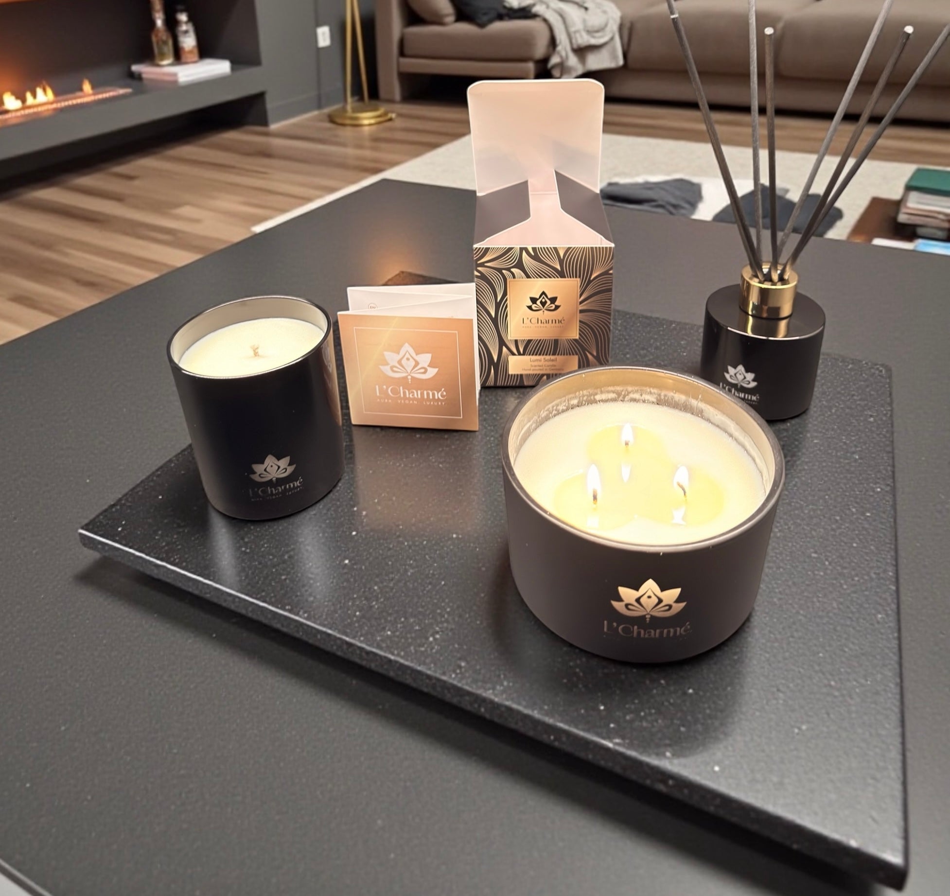 Duftkerzen und Duftstäbchen von L’Charmé mit Verpackung auf einer schwarzen Platte in einem eleganten Wohnraum