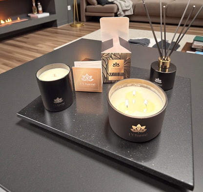 Duftkerzen und Duftstäbchen von L’Charmé mit Verpackung auf einer schwarzen Platte in einem eleganten Wohnraum