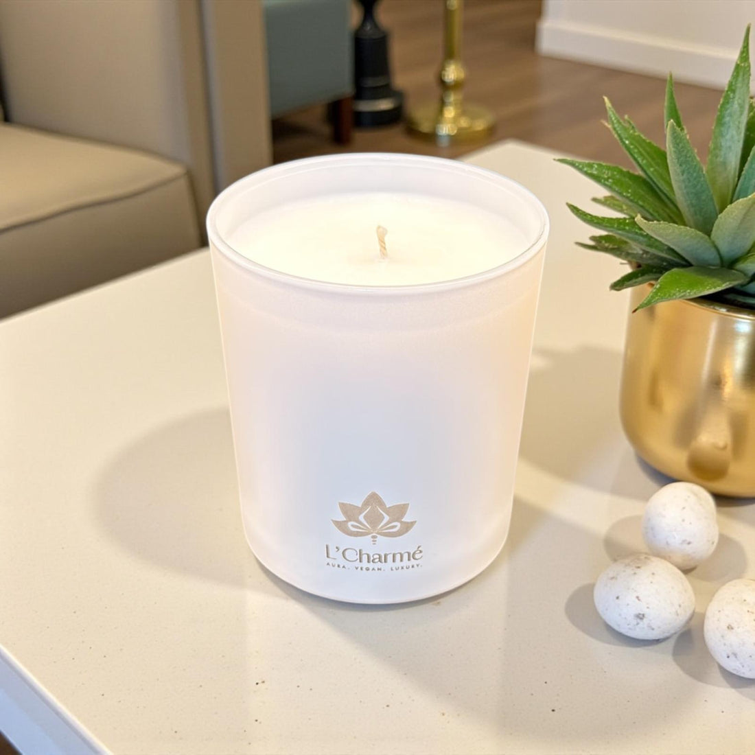 L’Charmé Duftkerze in Creme im modernen Wohnzimmer neben Sukkulente im Goldtopf.