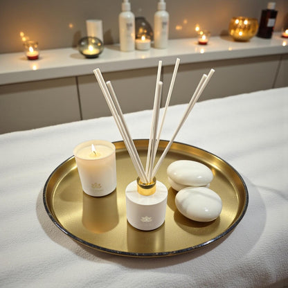 Raumduft Diffuser und Duftkerze auf goldenem Tablett mit weißen Steinen in ruhigem Wellness-Ambiente.