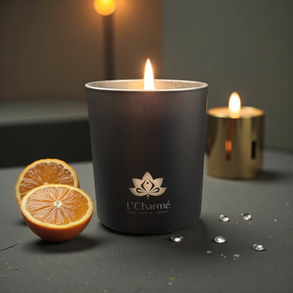 Schwarze brennende Duftkerze Mandarine Éclat von L’Charmé auf dunkler Oberfläche mit Orangenscheiben in elegantem Ambiente