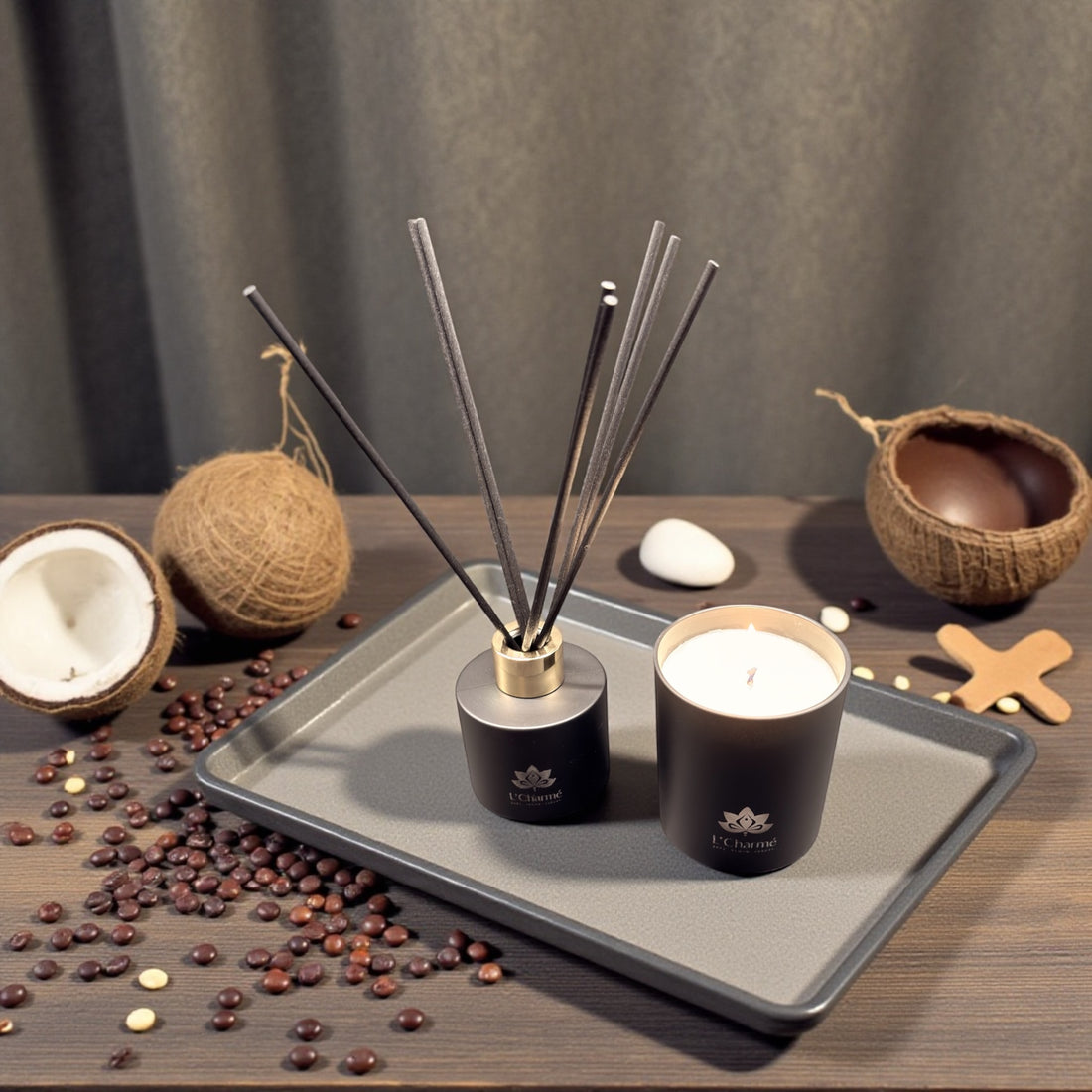 Schwarzer Duftdiffuser und brennende Duftkerze von L’Charmé auf einem grauen Tablett mit Kokosnuss und Kaffeebohnen in elegantem Arrangement