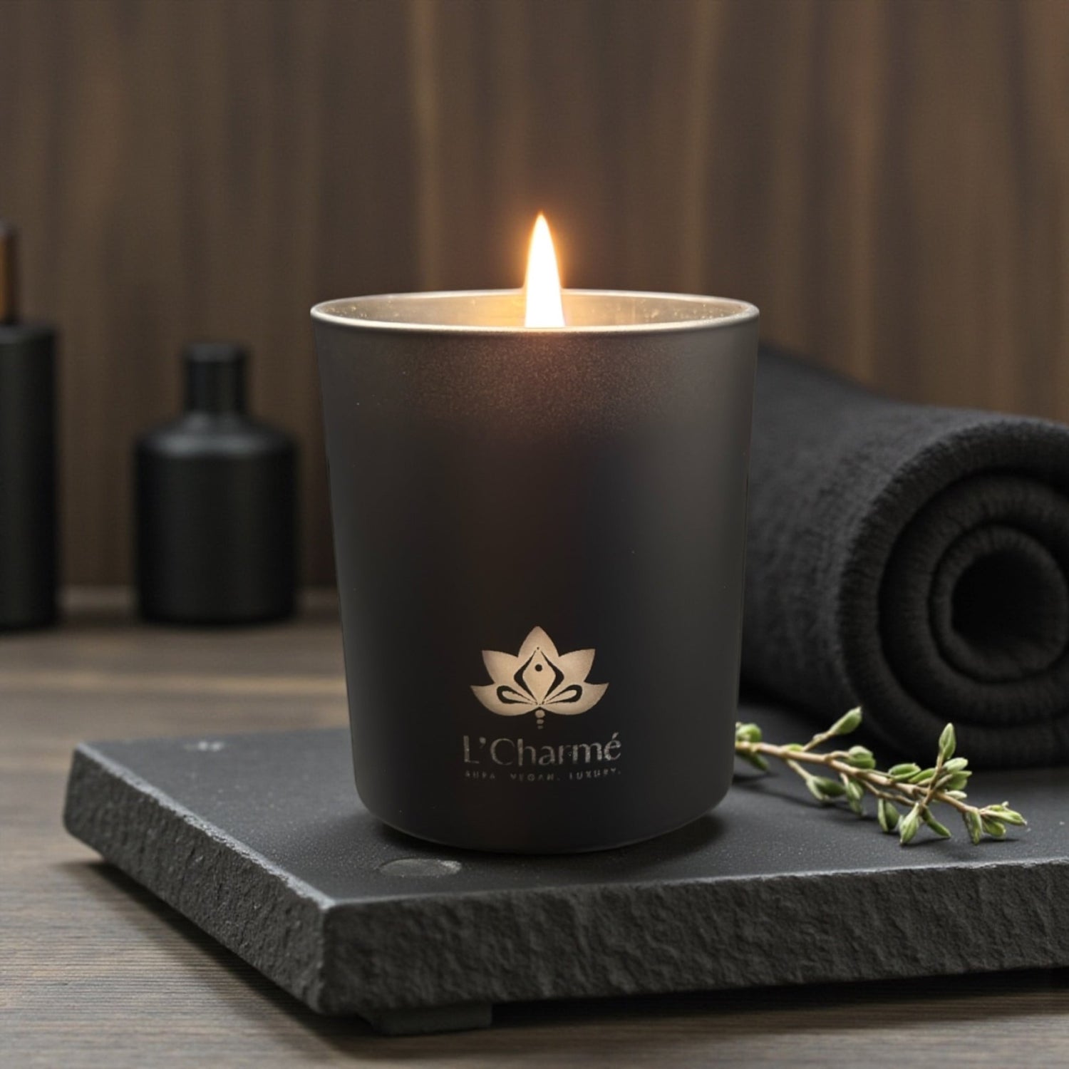 Schwarze Duftkerze von L’Charmé auf einer schwarzen Steinplatte im eleganten Spa-Ambiente