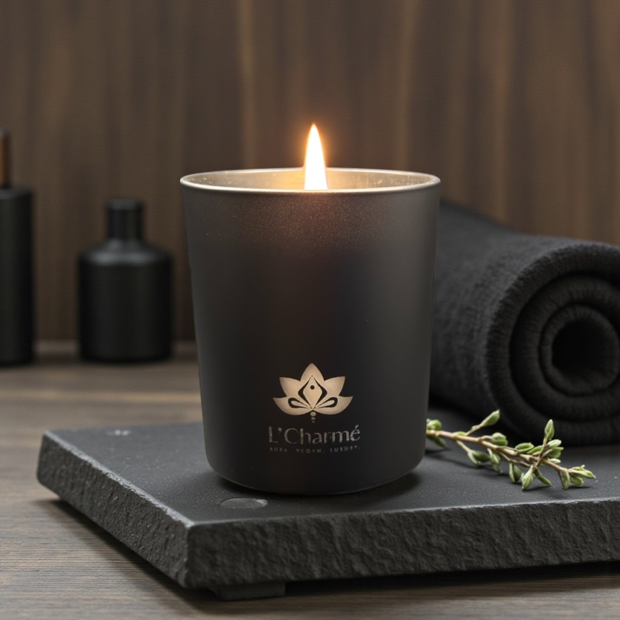 Schwarze Duftkerze von L’Charmé auf einer schwarzen Steinplatte im eleganten Spa-Ambiente