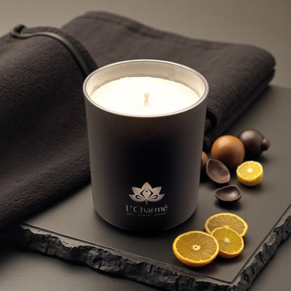 Schwarze Duftkerze von L’Charmé auf einer schwarzen Steinplatte mit Zitrusfrüchten in elegantem Arrangement