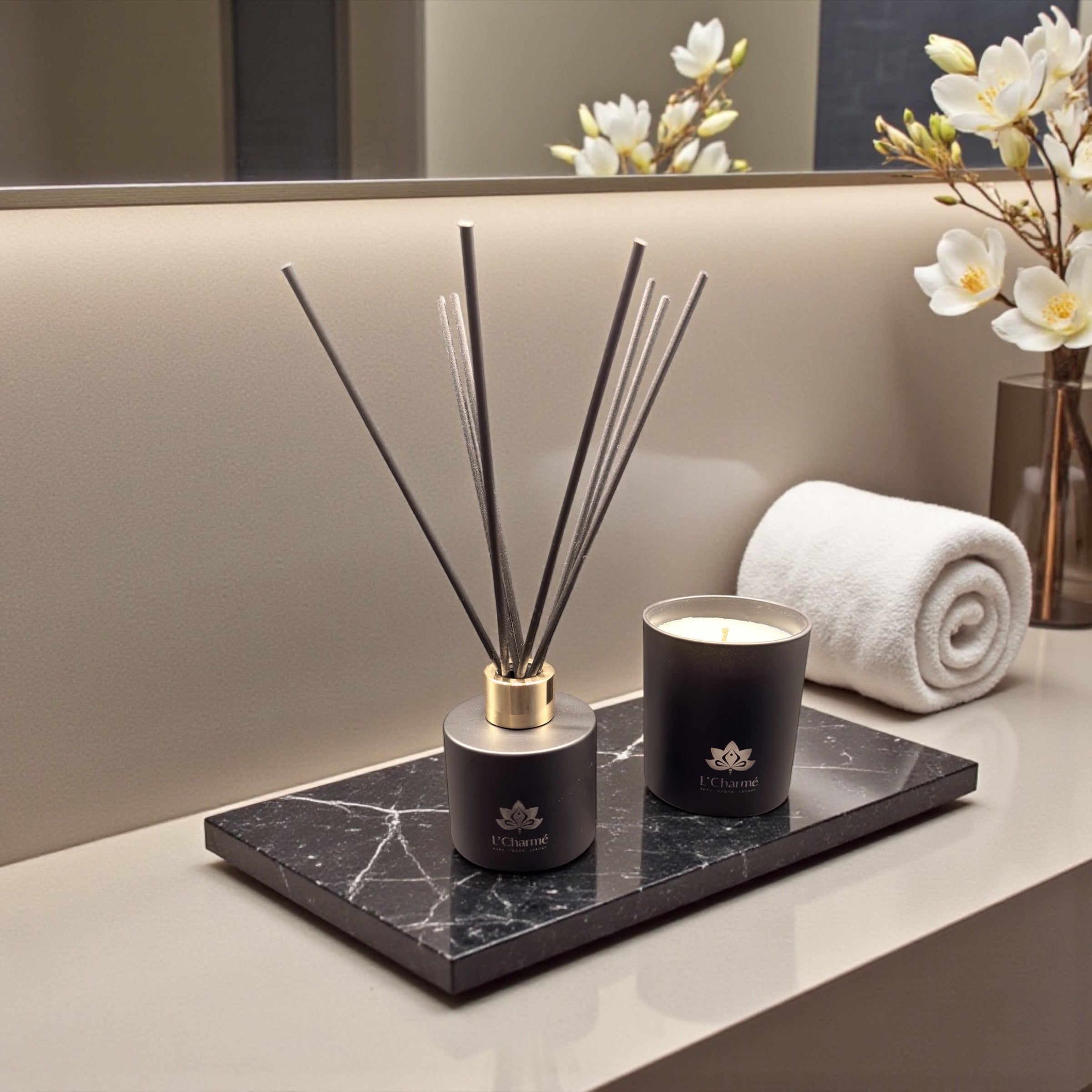 Schwarzer Duftdiffuser und Duftkerze von L’Charmé auf einer schwarzen Marmorplatte im eleganten Badezimmer mit weißem Handtuch und Blütenzweigen