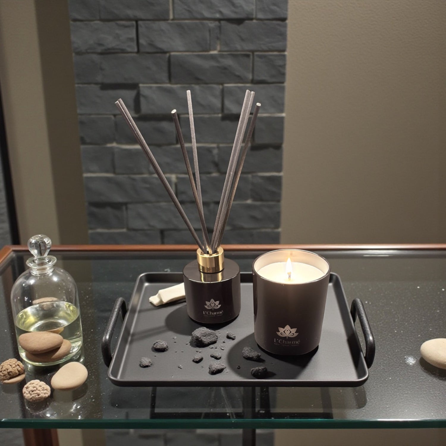 Schwarzer Duftdiffuser und brennende Duftkerze von L’Charmé auf einem schwarzen Tablett mit Steinen in elegantem Ambiente