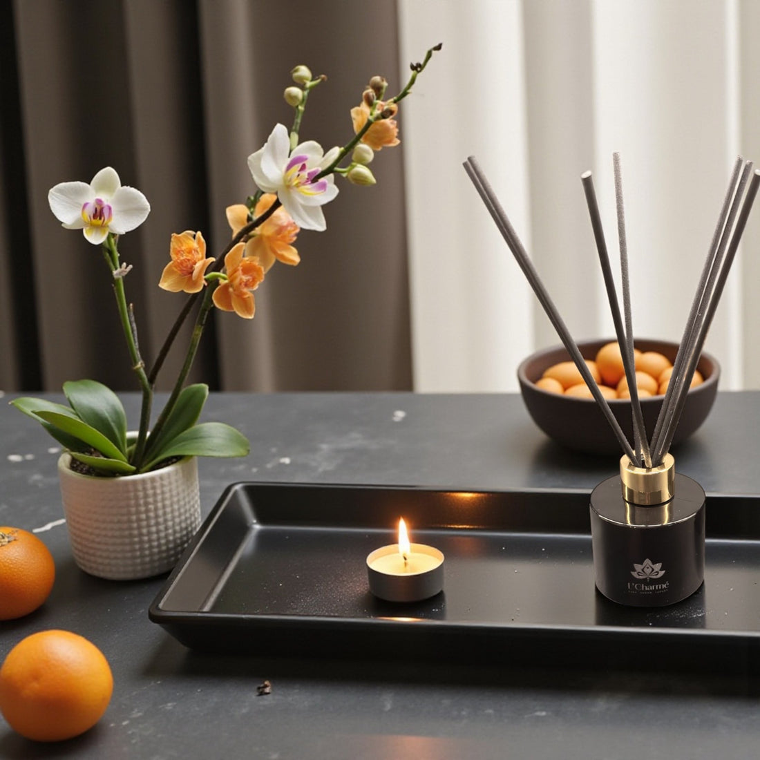 Schwarzer Duftdiffuser und Duftkerze von L’Charmé auf einer schwarzen Steinplatte in elegantem Arrangement