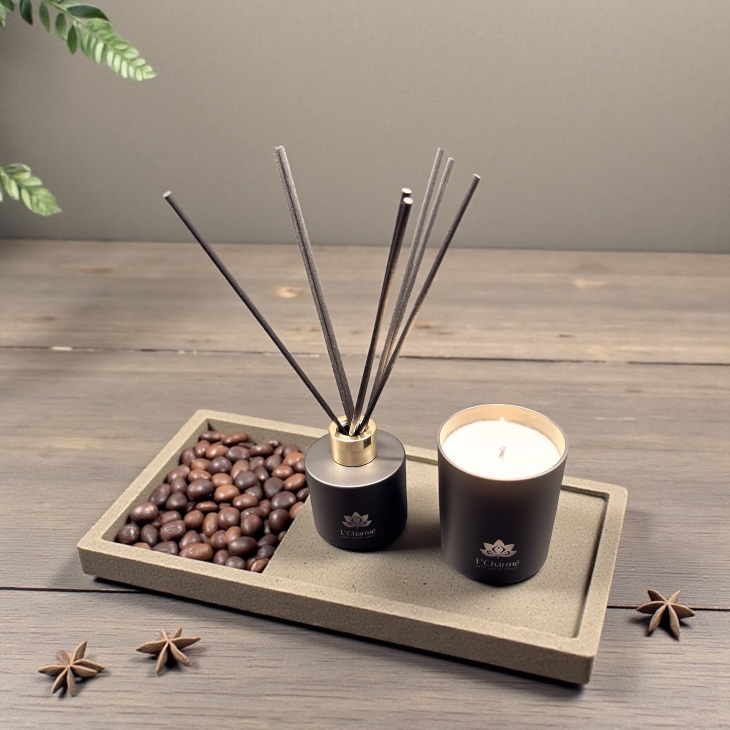 Schwarzer Duftdiffuser und brennende Duftkerze von L’Charmé auf einer Steinplatte mit Kaffeebohnen und Sternanis in elegantem Arrangement