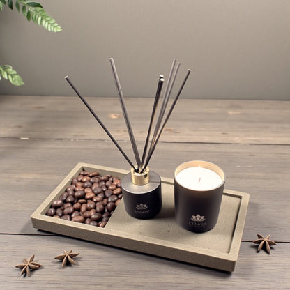 Schwarzer Duftdiffuser und brennende Duftkerze von L’Charmé auf einer Steinplatte mit Kaffeebohnen und Sternanis in elegantem Arrangement