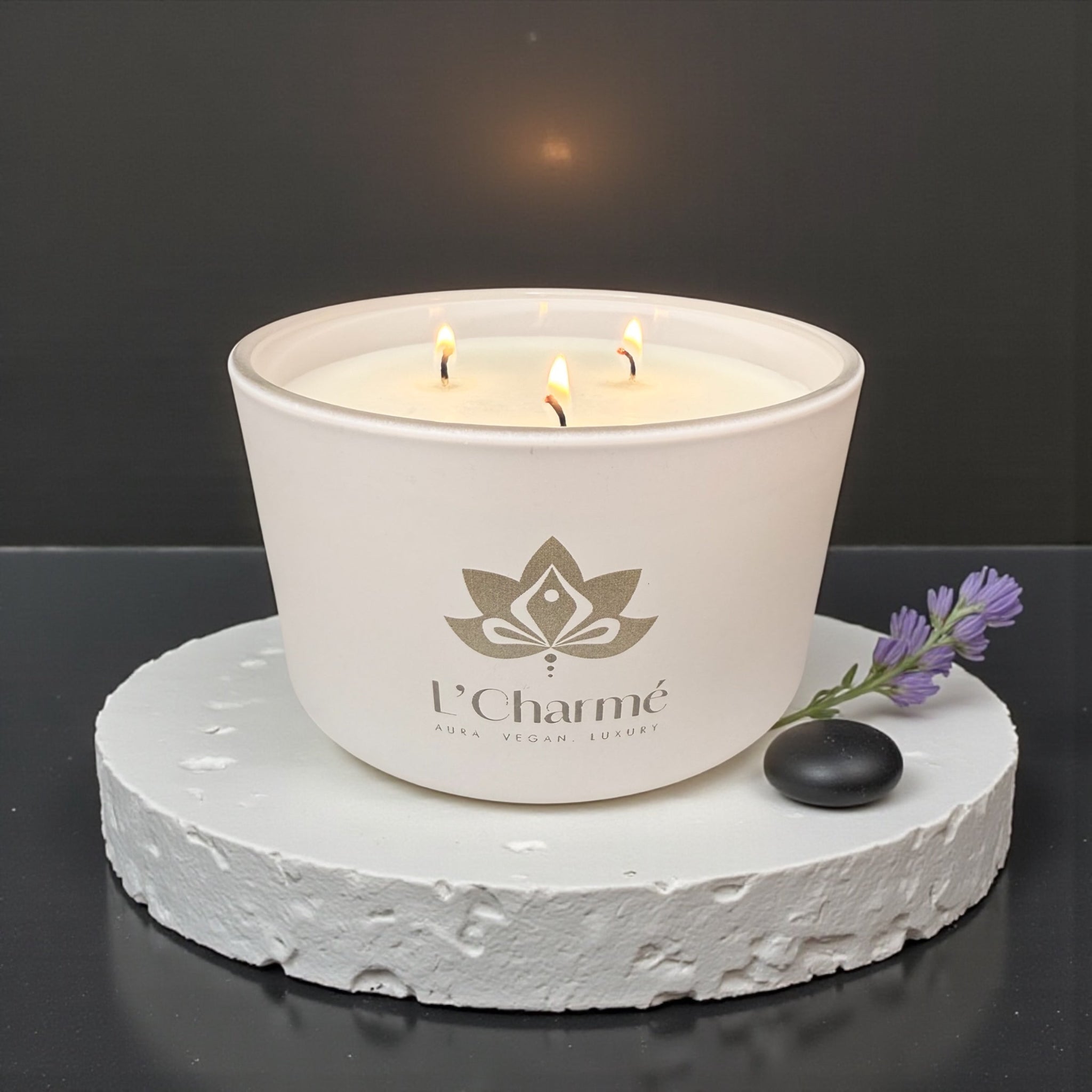 Weiße Dreidocht-Duftkerze von L’Charmé auf einer weißen Steinplatte mit Lavendel und schwarzem Dekostein in elegantem Ambiente