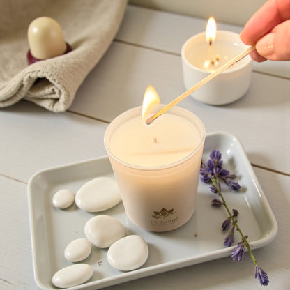 Weiße brennende Duftkerze von L’Charmé auf einem weißen Tablett mit Lavendel und weißen Steinen, während sie angezündet wird