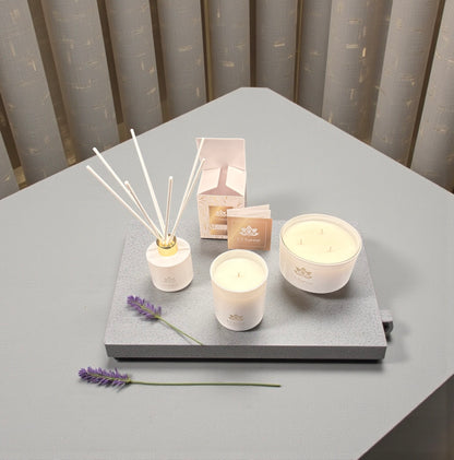 Weiße Duftkerzen und Duftstäbchen von L’Charmé mit Verpackung auf einer grauen Platte mit Lavendel in elegantem Arrangement