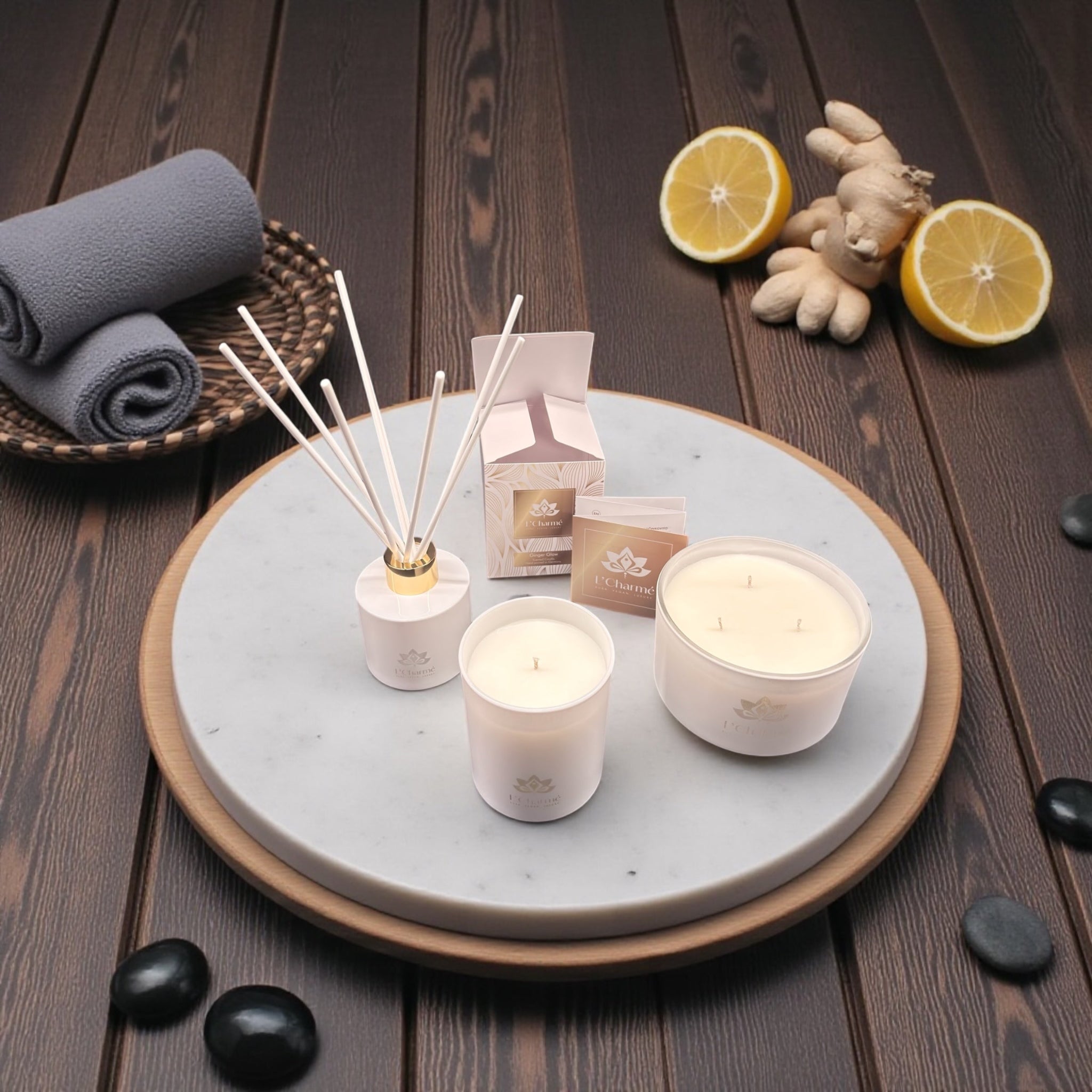 Weiße Duftkerzen und Duftstäbchen von L’Charmé mit Verpackung auf einer runden Marmorplatte mit Ingwer und Zitronen in elegantem Spa-Ambiente