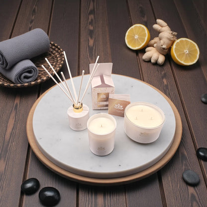 Weiße Duftkerzen und Duftstäbchen von L’Charmé mit Verpackung auf einer runden Marmorplatte mit Ingwer und Zitronen in elegantem Spa-Ambiente