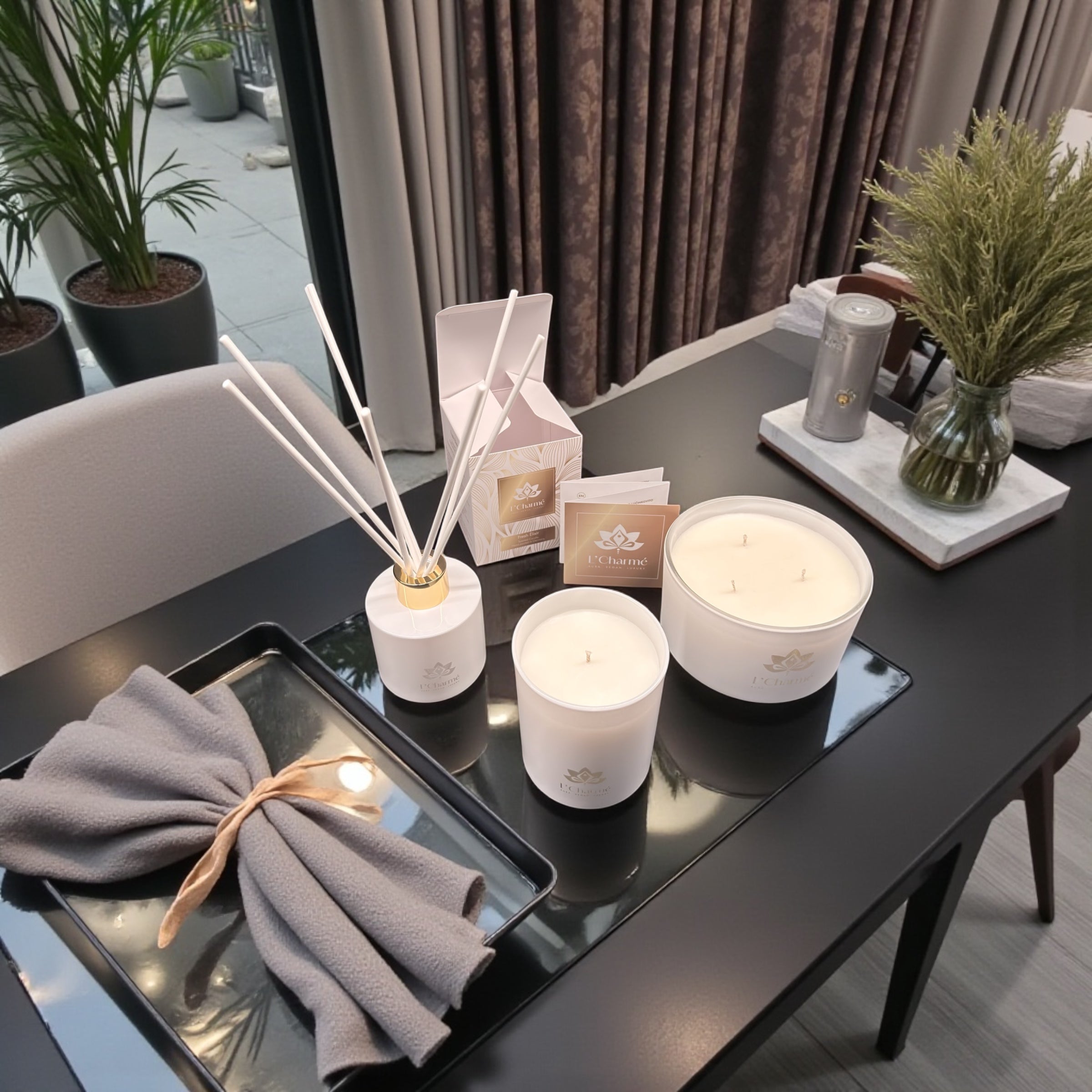 Weiße Duftkerzen und Duftstäbchen von L’Charmé mit Verpackung auf einem schwarzen Tisch in elegantem Wohnambiente