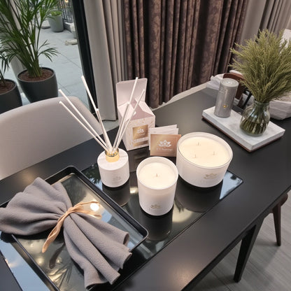 Weiße Duftkerzen und Duftstäbchen von L’Charmé mit Verpackung auf einem schwarzen Tisch in elegantem Wohnambiente