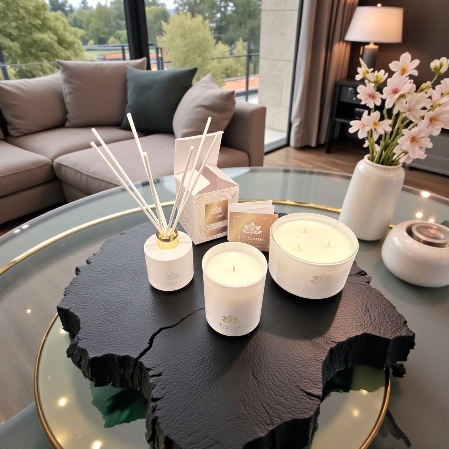 Weiße Duftkerzen und Duftstäbchen von L’Charmé mit Verpackung auf einer schwarzen Natursteinplatte in elegantem Wohnambiente