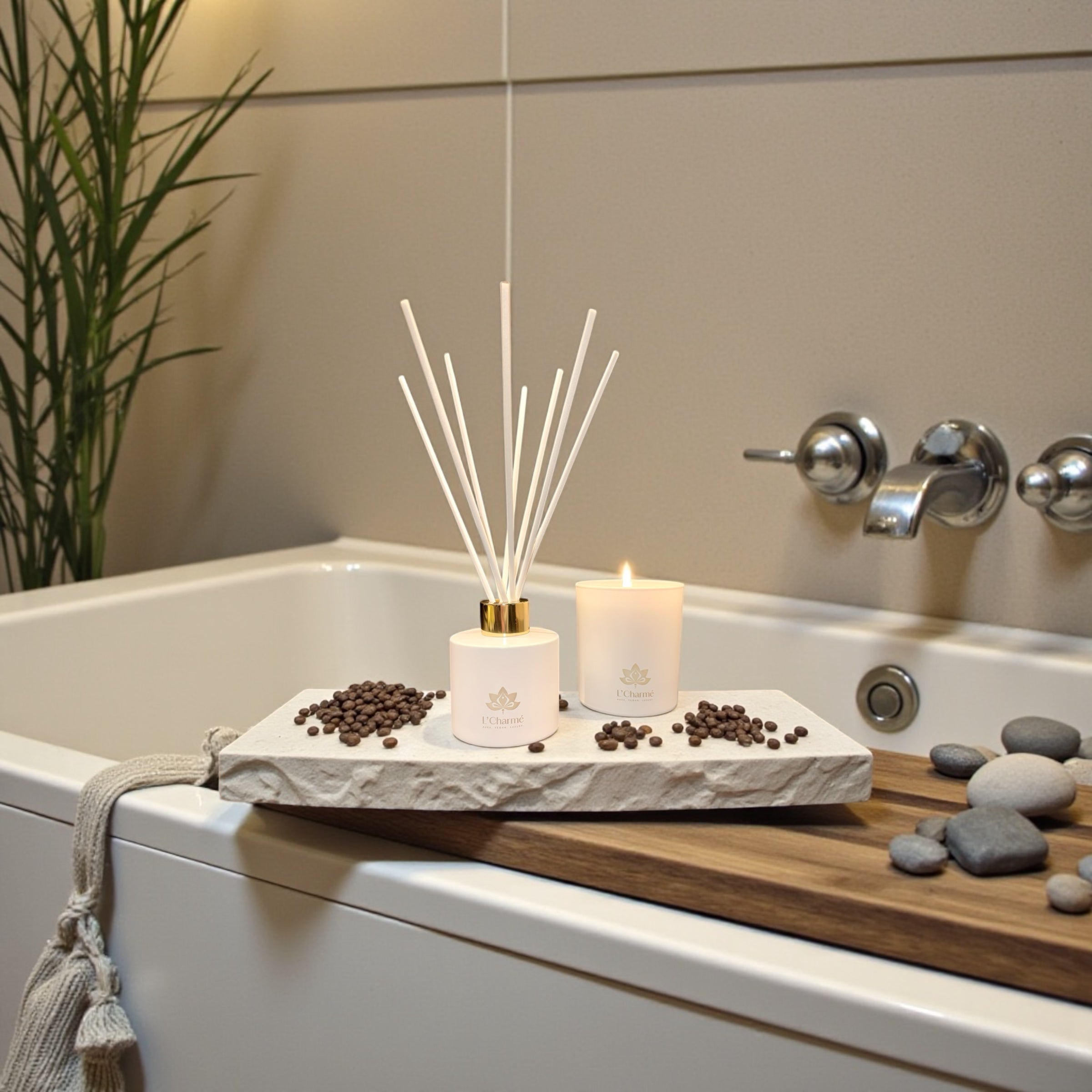 Weißer Duftdiffuser und brennende Duftkerze von L’Charmé auf einer Steinplatte an der Badewanne in ruhigem Spa-Ambiente